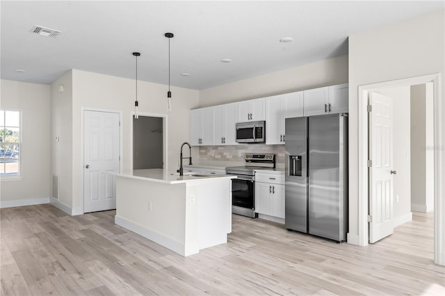 kitchen with appliances with stainless steel finishes, decorative light fixtures, light hardwood / wood-style floors, and an island with sink