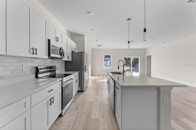 kitchen featuring white cabinets, a center island with sink, sink, appliances with stainless steel finishes, and decorative light fixtures