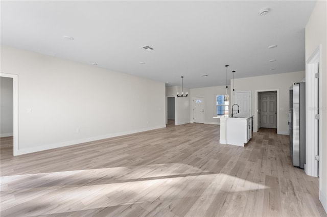 unfurnished living room featuring light hardwood / wood-style flooring, a chandelier, and sink