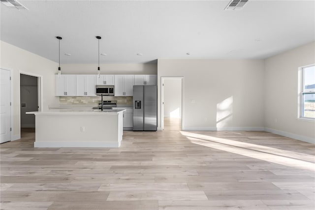 kitchen with pendant lighting, decorative backsplash, an island with sink, appliances with stainless steel finishes, and white cabinetry