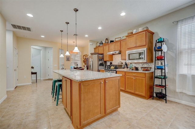 kitchen with pendant lighting, an island with sink, appliances with stainless steel finishes, tasteful backsplash, and light tile patterned flooring