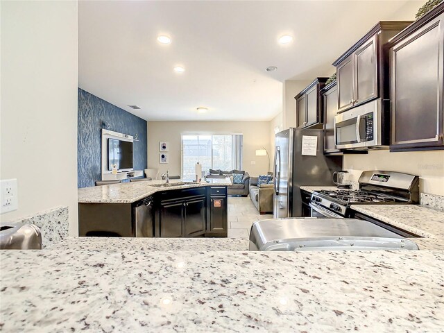 kitchen with light stone countertops, sink, stainless steel appliances, kitchen peninsula, and dark brown cabinets