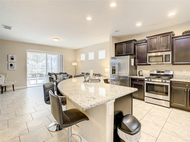 5303 Wildwood Way, Davenport, FL 33837 - kitchen with appliances with stainless steel finishes, a breakfast bar area, light stone counters, light tile patterned floors, and dark brown cabinets