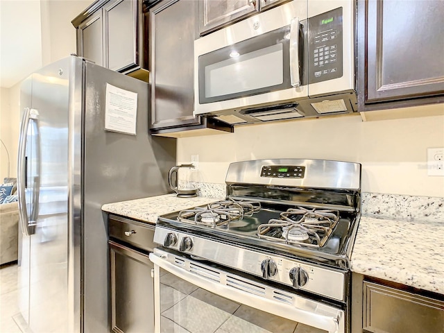 5303 Wildwood Way, Davenport, FL 33837 - kitchen featuring appliances with stainless steel finishes, light tile patterned floors, dark brown cabinets, and light stone countertops