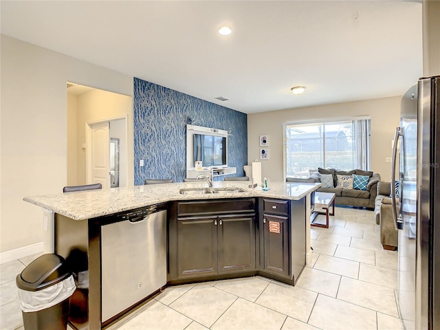 kitchen featuring a kitchen island with sink, sink, stainless steel appliances, and light stone counters