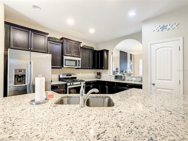 kitchen with dark brown cabinets, sink, light stone countertops, and stainless steel appliances