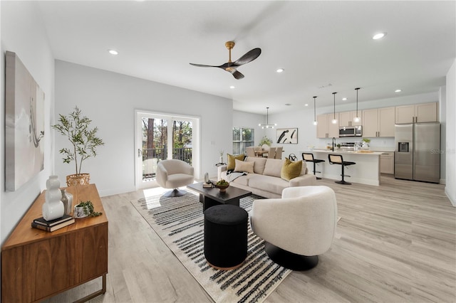 living room with ceiling fan with notable chandelier and light hardwood / wood-style floors