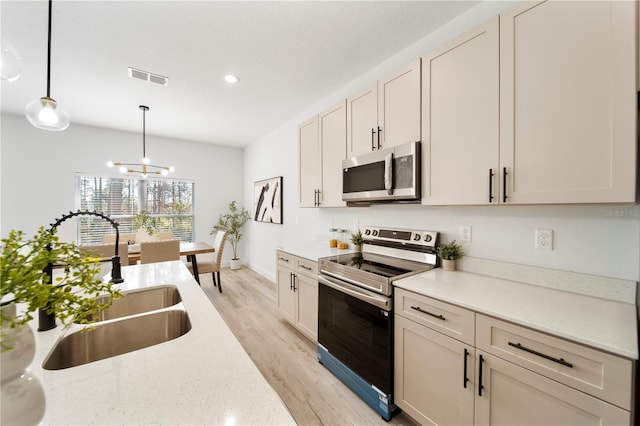 kitchen with appliances with stainless steel finishes, light stone counters, sink, light hardwood / wood-style floors, and hanging light fixtures