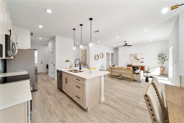 kitchen with light wood-type flooring, stainless steel appliances, a kitchen island with sink, sink, and pendant lighting