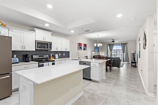 kitchen with kitchen peninsula, appliances with stainless steel finishes, ceiling fan with notable chandelier, sink, and a center island