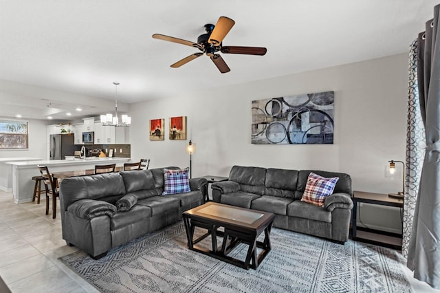 tiled living room featuring ceiling fan with notable chandelier and sink