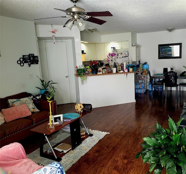 living room with a textured ceiling, ceiling fan, and dark wood-type flooring