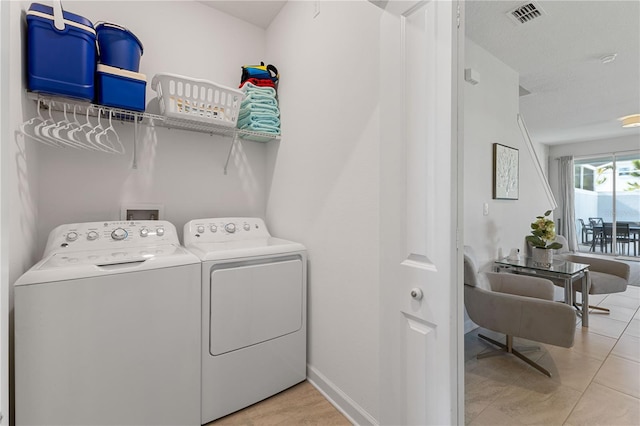 clothes washing area featuring washer and dryer, light tile patterned flooring, and a textured ceiling