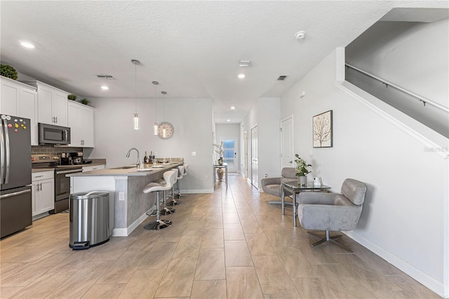 kitchen featuring pendant lighting, a kitchen island with sink, white cabinets, a kitchen breakfast bar, and appliances with stainless steel finishes