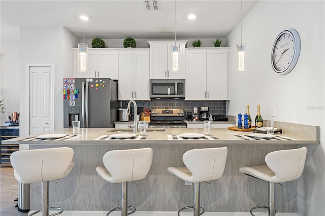 kitchen with white cabinets, appliances with stainless steel finishes, a breakfast bar, and decorative light fixtures