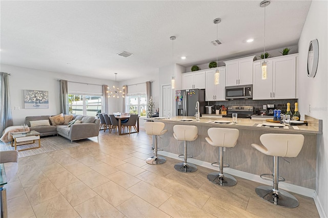 kitchen with a breakfast bar, white cabinets, decorative backsplash, decorative light fixtures, and stainless steel appliances