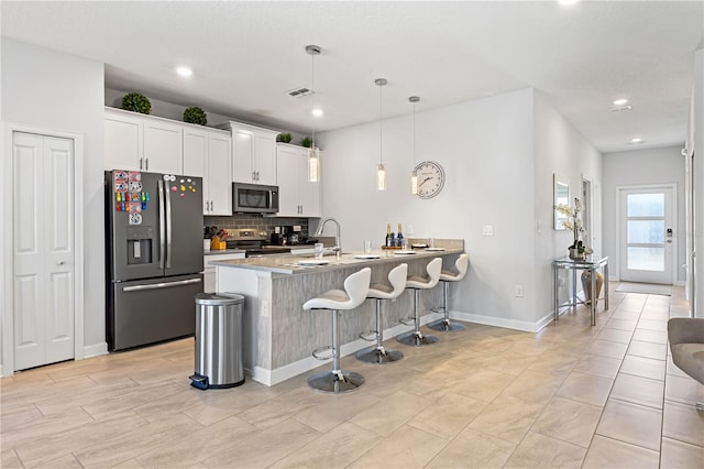 kitchen with a kitchen bar, appliances with stainless steel finishes, sink, pendant lighting, and white cabinetry