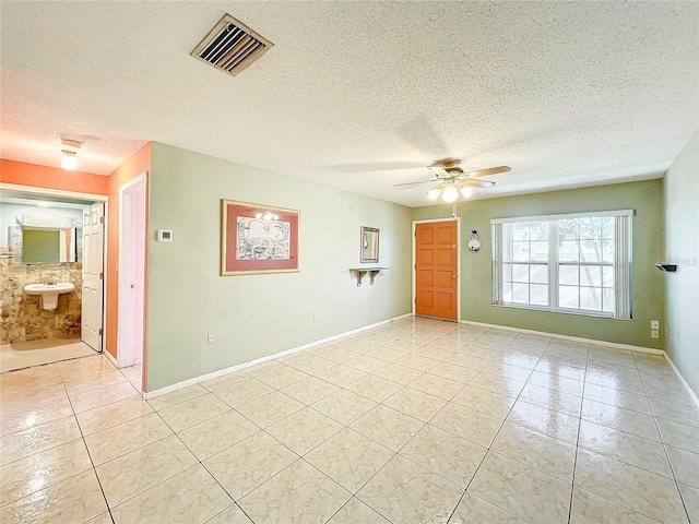 tiled spare room with ceiling fan, sink, and a textured ceiling