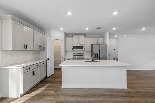 kitchen featuring decorative backsplash, stainless steel appliances, dark wood-type flooring, and an island with sink