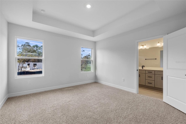 unfurnished bedroom with a raised ceiling, multiple windows, and ensuite bath