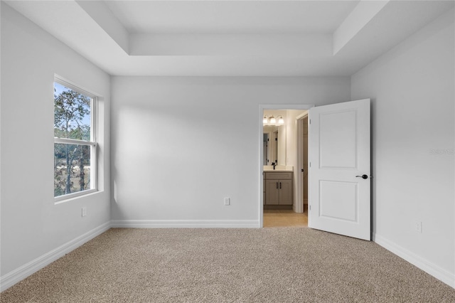 unfurnished bedroom with a raised ceiling, connected bathroom, and light carpet