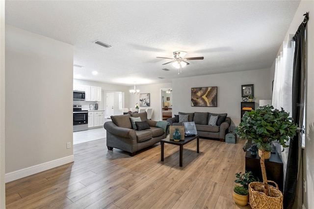 living room featuring a textured ceiling, ceiling fan with notable chandelier, and light wood-type flooring