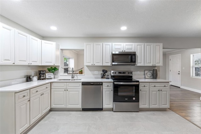 kitchen featuring appliances with stainless steel finishes, light wood-type flooring, a textured ceiling, sink, and white cabinetry