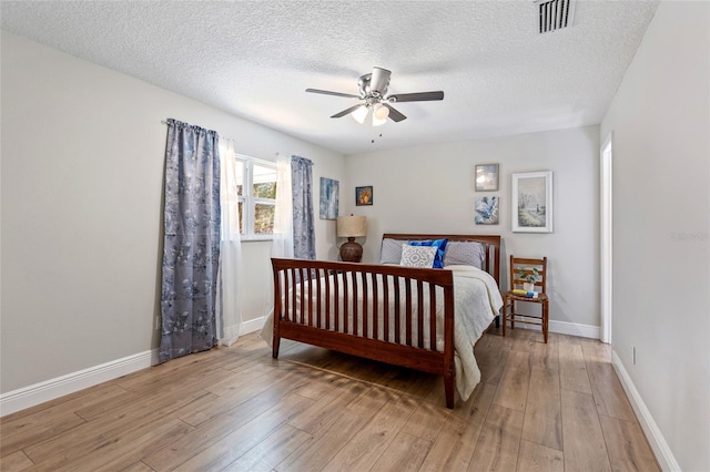 bedroom with a textured ceiling, light wood-type flooring, and ceiling fan