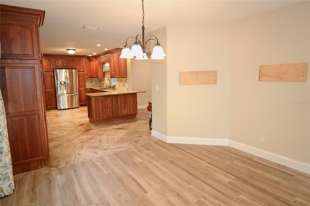 kitchen with light stone countertops, stainless steel fridge, light wood-type flooring, and hanging light fixtures