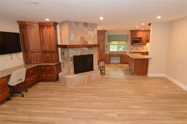 living room with a stone fireplace, built in desk, and light hardwood / wood-style floors