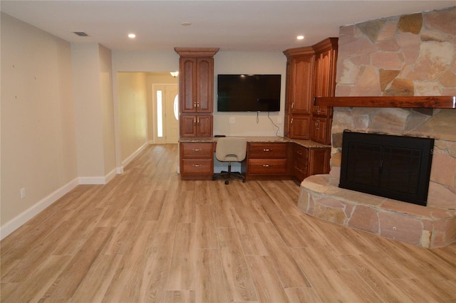 unfurnished living room featuring a stone fireplace, light wood-type flooring, and built in desk