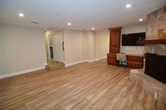 living room featuring light hardwood / wood-style floors, a stone fireplace, and built in desk