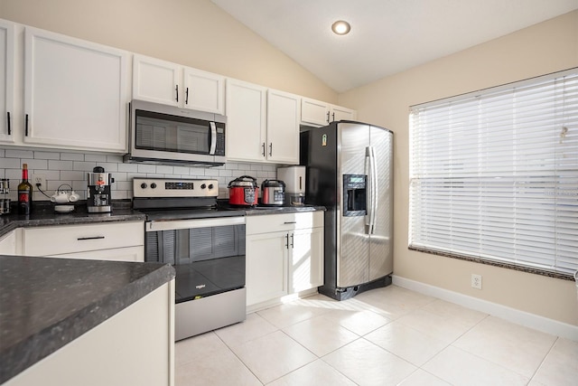 kitchen featuring appliances with stainless steel finishes, backsplash, vaulted ceiling, light tile patterned floors, and white cabinetry