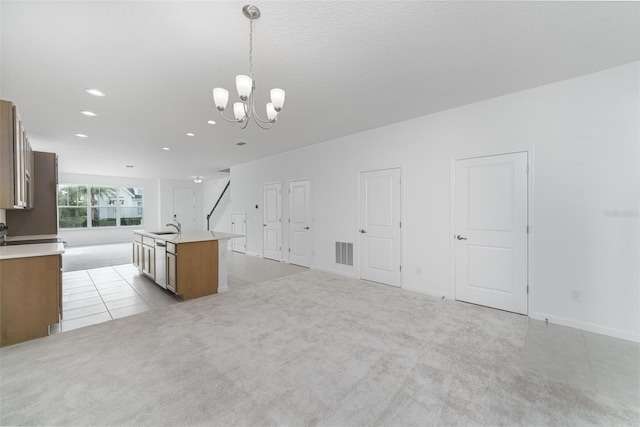 kitchen with pendant lighting, stainless steel dishwasher, an island with sink, a notable chandelier, and light colored carpet