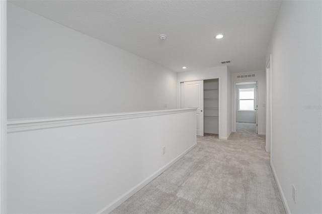 hall with light colored carpet and a textured ceiling