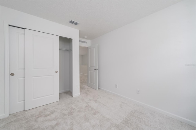 unfurnished bedroom featuring light colored carpet, a textured ceiling, and a closet