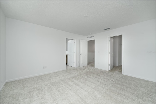 unfurnished bedroom featuring a textured ceiling, a spacious closet, light carpet, and a closet