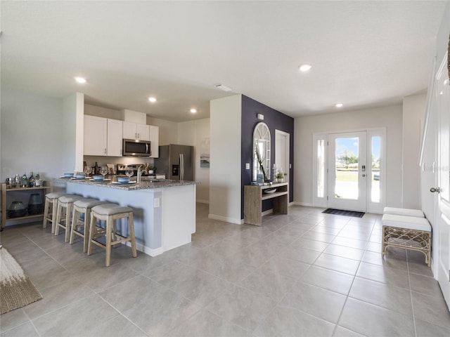 kitchen with stainless steel appliances, kitchen peninsula, dark stone counters, a kitchen bar, and white cabinets