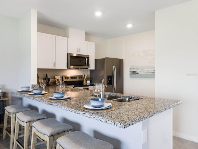 kitchen featuring kitchen peninsula, a breakfast bar, stainless steel appliances, and white cabinets