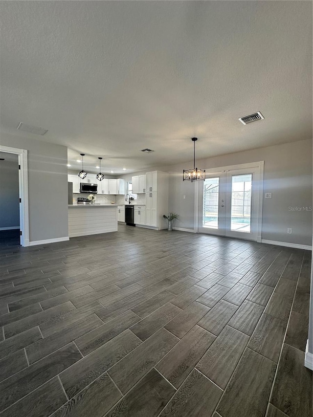 unfurnished living room featuring a chandelier, french doors, dark wood-type flooring, and a textured ceiling