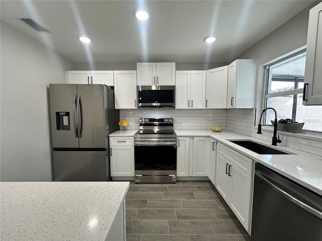 kitchen with white cabinets, sink, decorative backsplash, light stone countertops, and appliances with stainless steel finishes