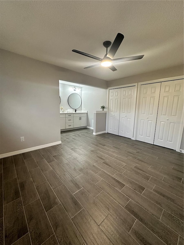 unfurnished bedroom featuring multiple closets, a textured ceiling, ceiling fan, and dark wood-type flooring