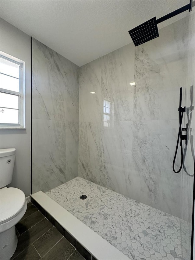 bathroom with a textured ceiling, toilet, and tiled shower