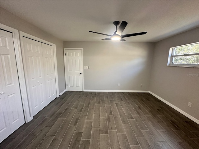 unfurnished bedroom featuring dark hardwood / wood-style flooring, ceiling fan, and multiple closets