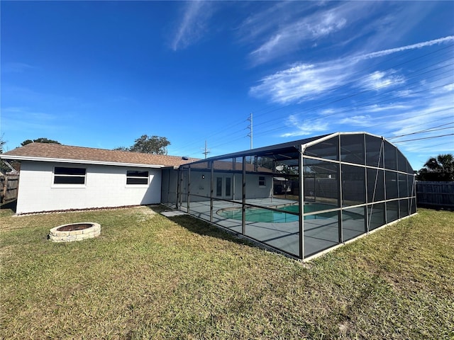 rear view of house with a lawn, glass enclosure, a fenced in pool, and an outdoor fire pit