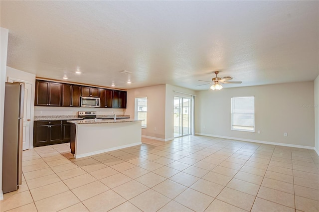 kitchen featuring appliances with stainless steel finishes, an island with sink, ceiling fan, dark brown cabinets, and light tile patterned flooring