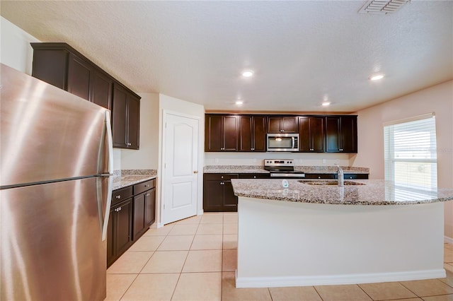 kitchen featuring appliances with stainless steel finishes, sink, light stone countertops, and a center island with sink