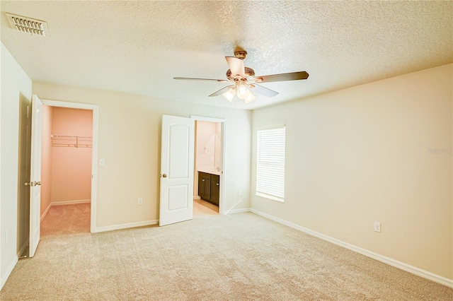 unfurnished bedroom with connected bathroom, a closet, light carpet, ceiling fan, and a spacious closet