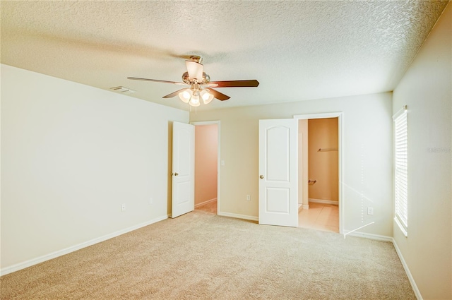 unfurnished bedroom featuring ensuite bath, light colored carpet, ceiling fan, a spacious closet, and a textured ceiling