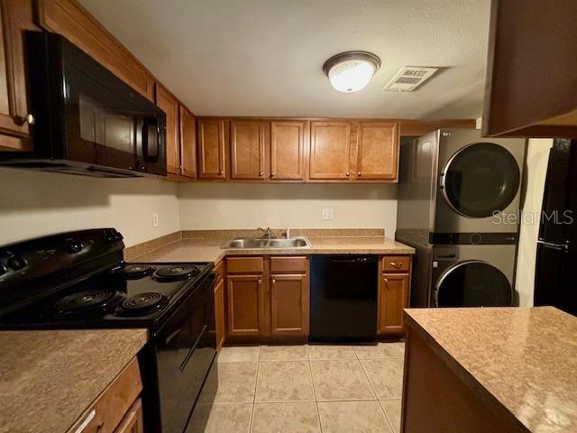 kitchen with black appliances, light tile patterned floors, sink, and stacked washer and clothes dryer